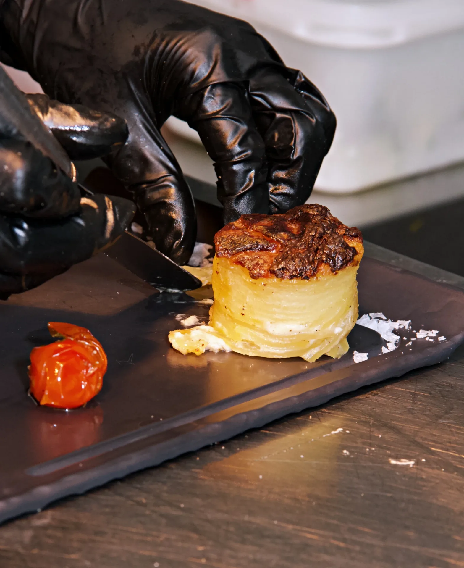 Chef emplatando una torre de patatas gratinadas y tomate asado en Le Gourmand Jávea